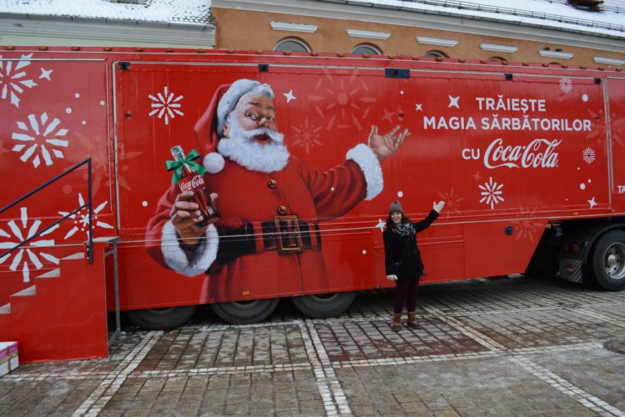 A woman poses in front of a big red photo of Santa.