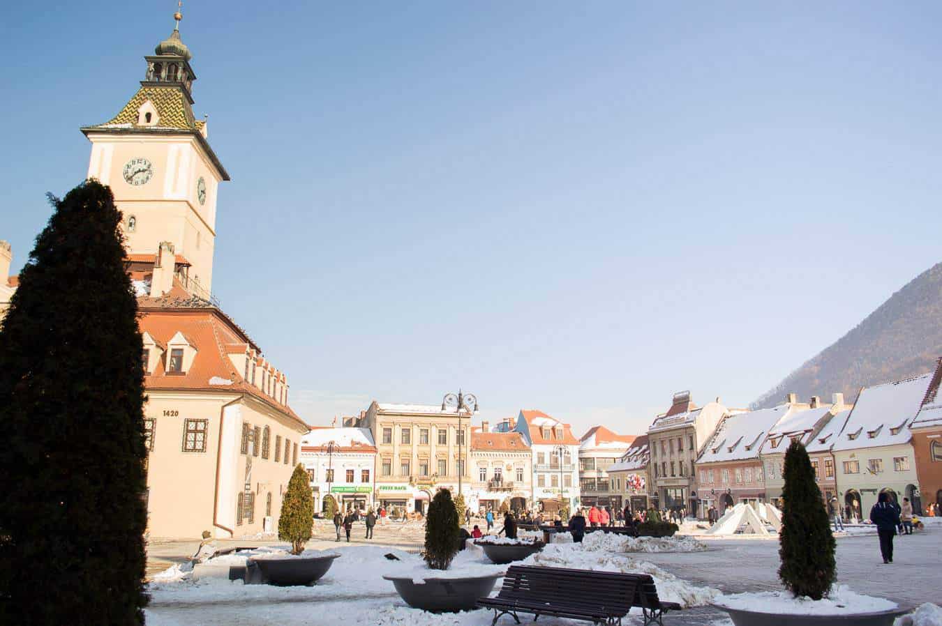 People wander around a snowy square surrounded by buildings.