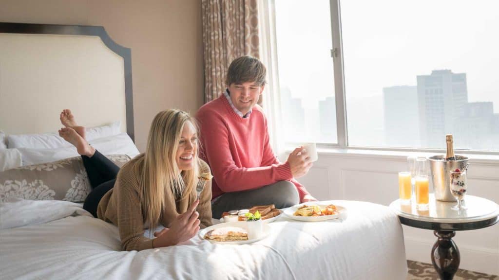 A couple eating breakfast in bed in a hotel room.