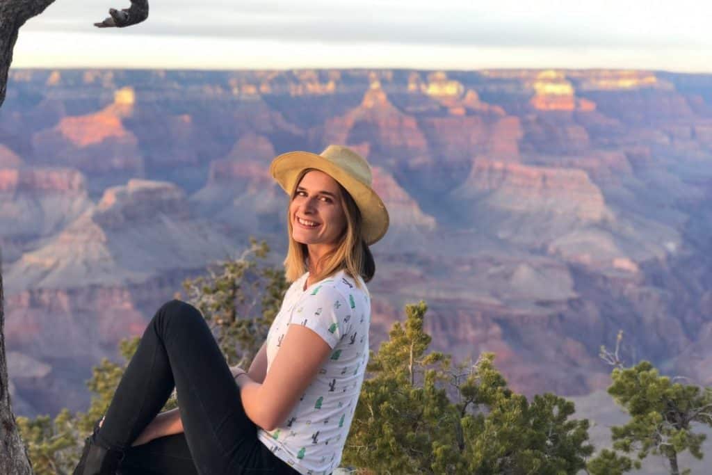 A woman sits in a hand smiling with a canyon behind her.