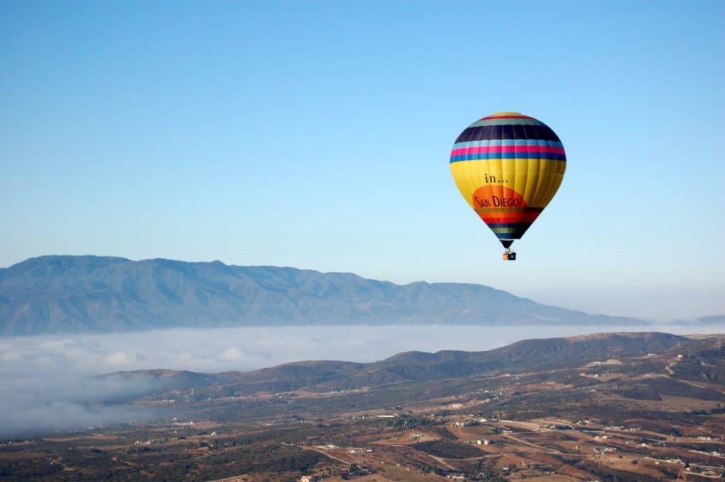 A hot air balloon over a town with mountains in the background.