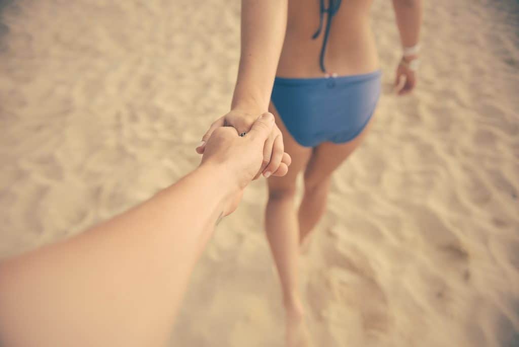 A person holds a woman\'s hands at the beach.