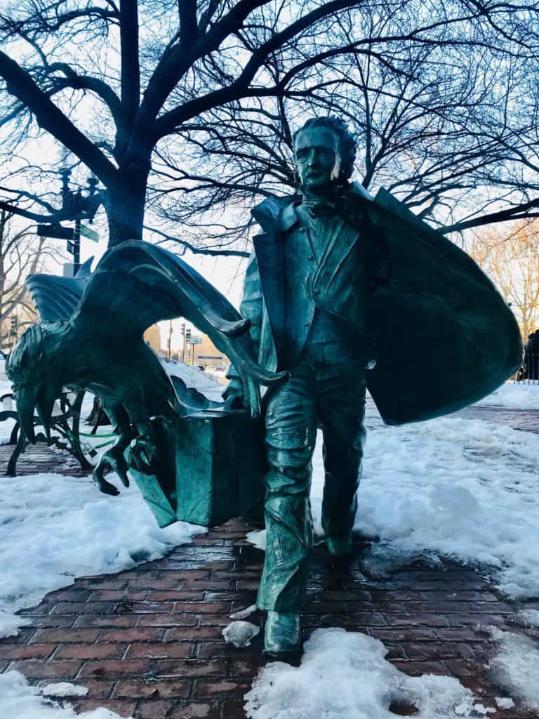 Green statue of a man walking and holding a suitcase with a bird flying out of it.