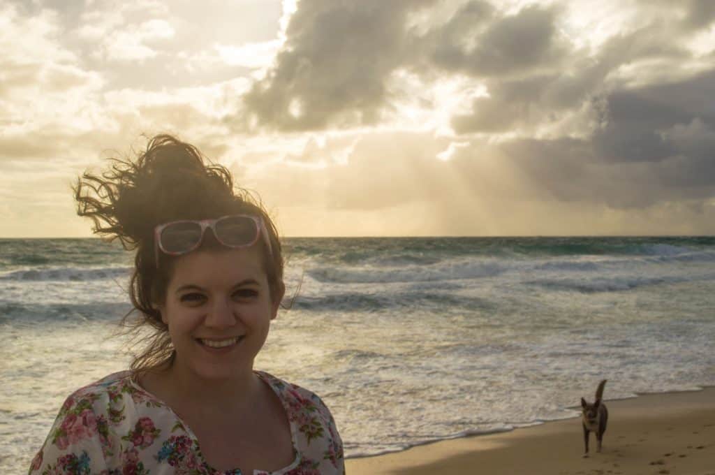 A woman smiles in front of a beach.