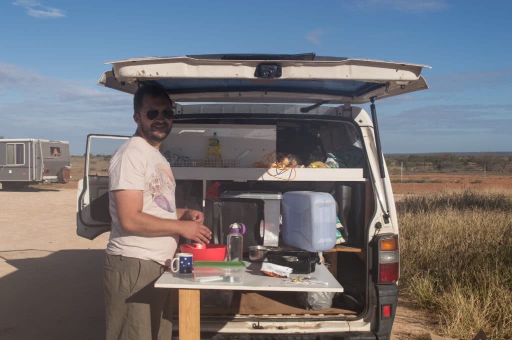 A guy makes dinner in the back of a campervan.