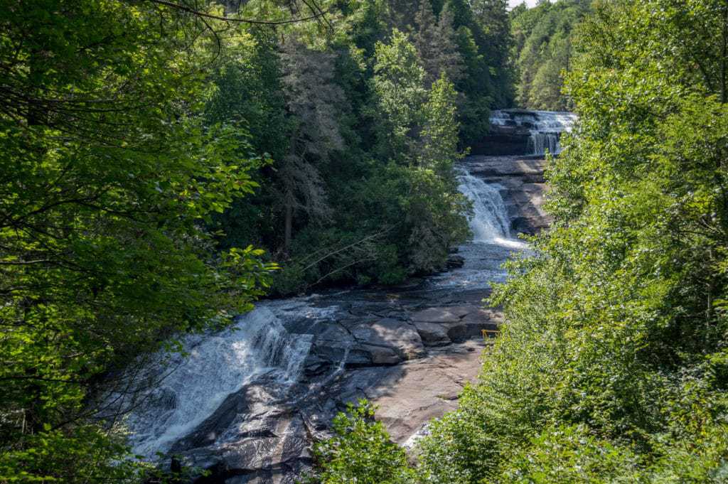 A long waterfall cascades down rocks surrounded by green forest.