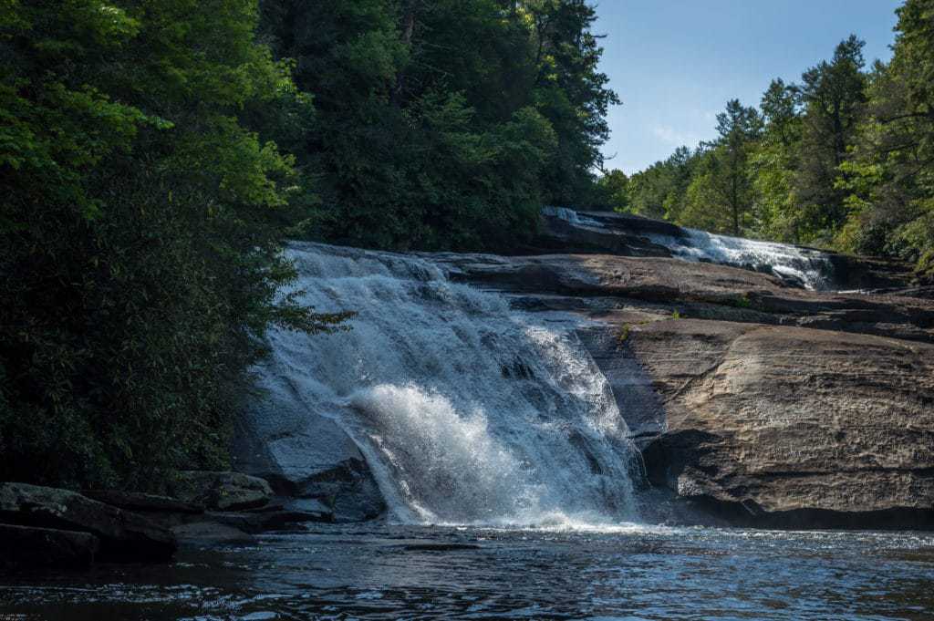 A waterfall cascades down rocks into a pool of water near trees.