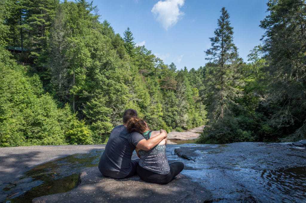 A couple sits together looking out at a forest.