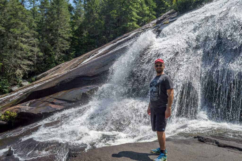 A man smiles while standing next to a waterfall.