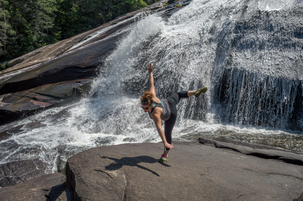 A woman does yoga next to a waterfall.