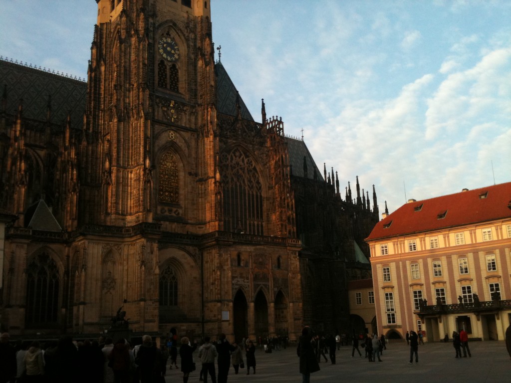 A large clock tower towering over a city and plaza where people are walking.