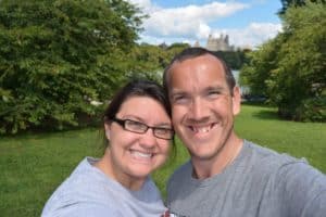 A couple smiling with a view of a castle in the distance behind them.