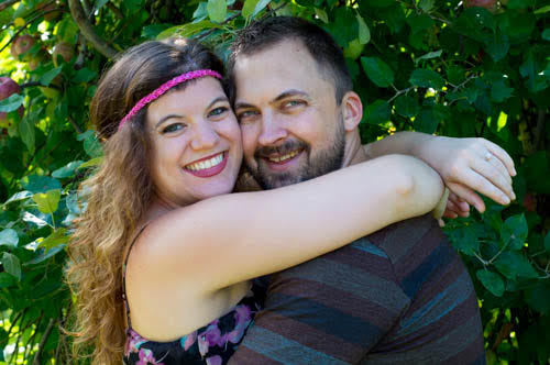A woman and a man hug each other smiling, with a tree behind them.