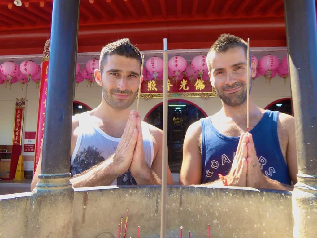 Two men each hold a stick in between their hands with pink lanterns hanging behind them.