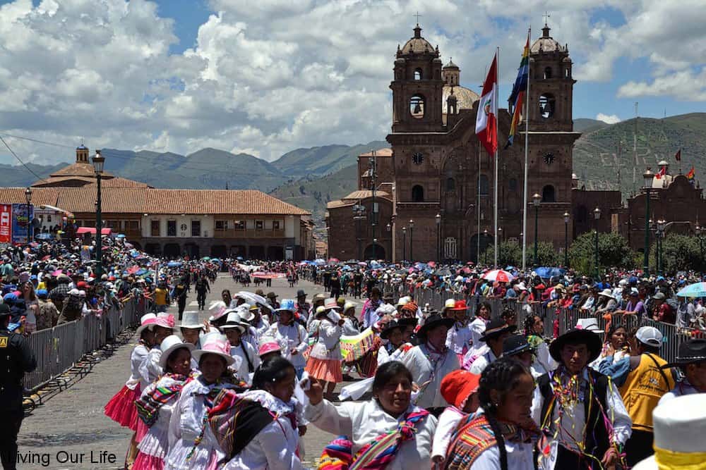 A group of people at a festival surrounded by historic buildings and mountains.