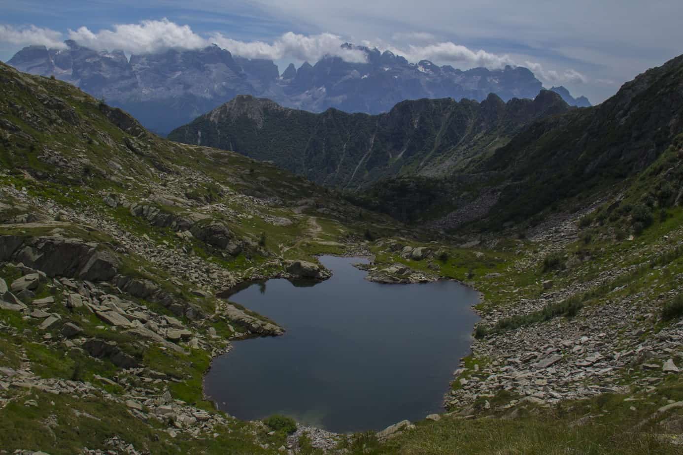 A peaceful pond sits surrounded by mountains. In the distance, smoke can be seen on the mountains.