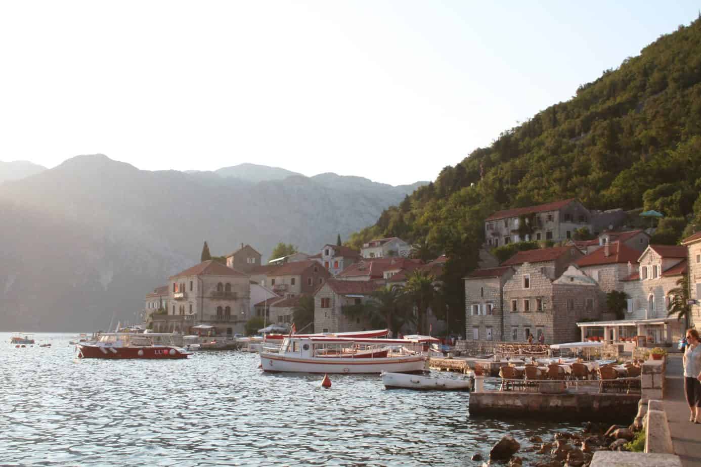 Boats float in the water next to buildings on the side of a mountain.