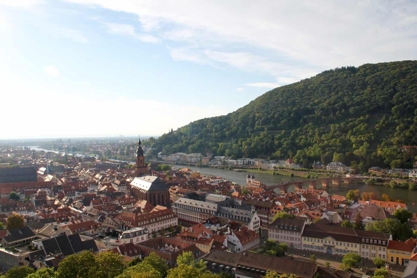 Aerial view of a historic town on a river next to a tall green mountain.