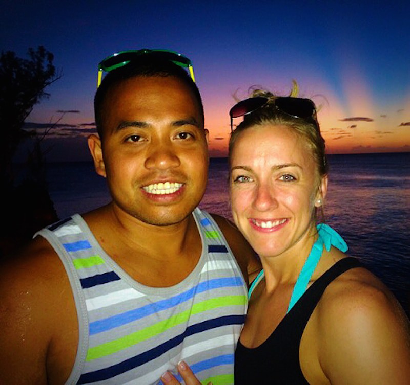 Man and woman smiling by the water with the sun setting above them.