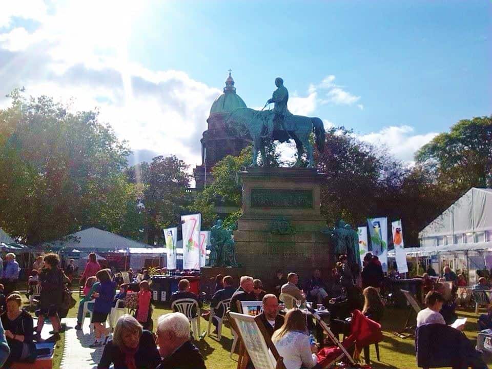 People sit in chairs outside around a sculpture of a man riding a horse.