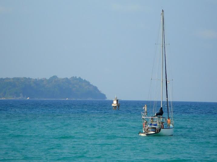 A boat floats on the blue ocean. A forest can be seen in the distance.