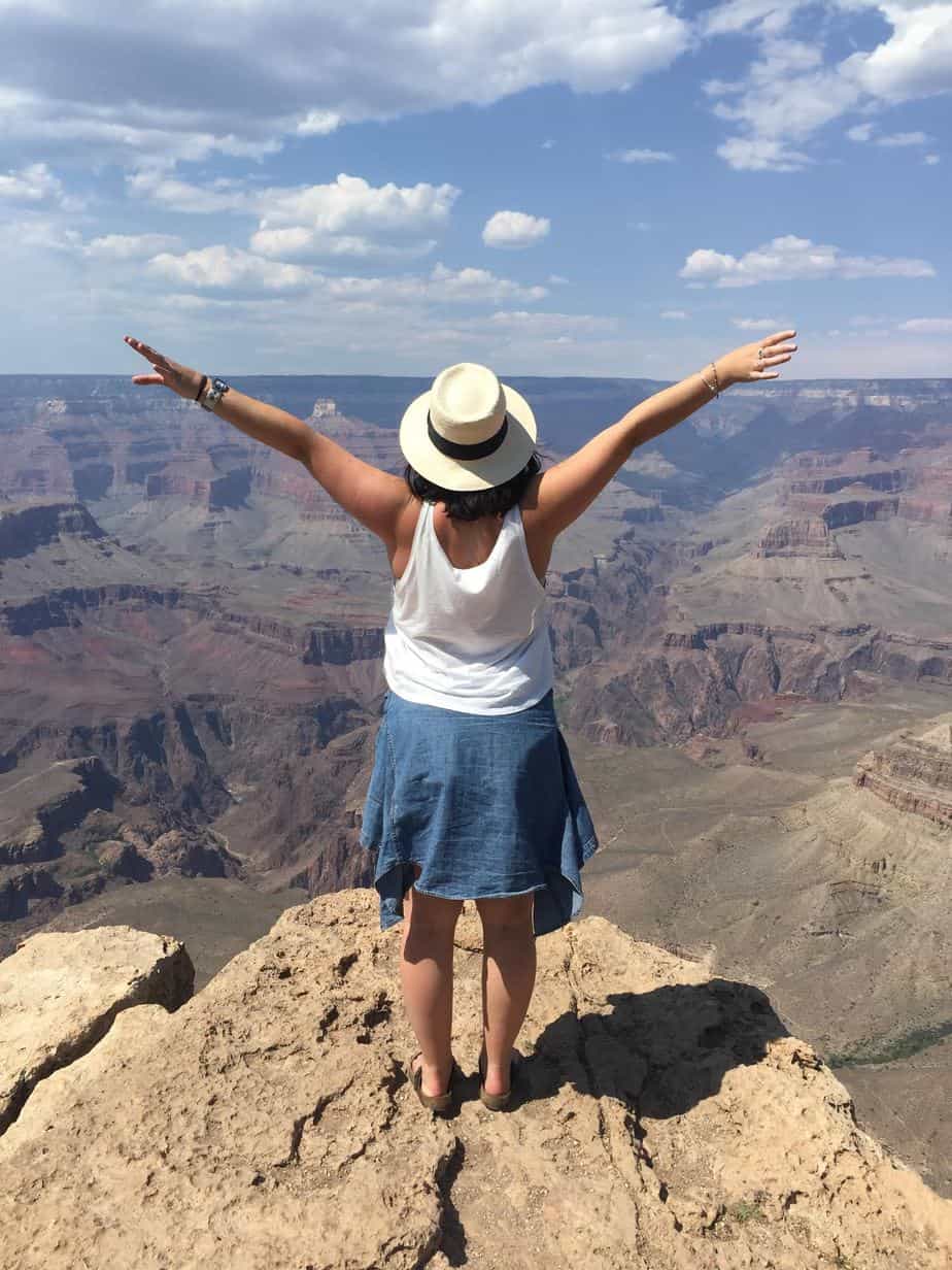 A woman stands with her arms up next to a huge canyon.