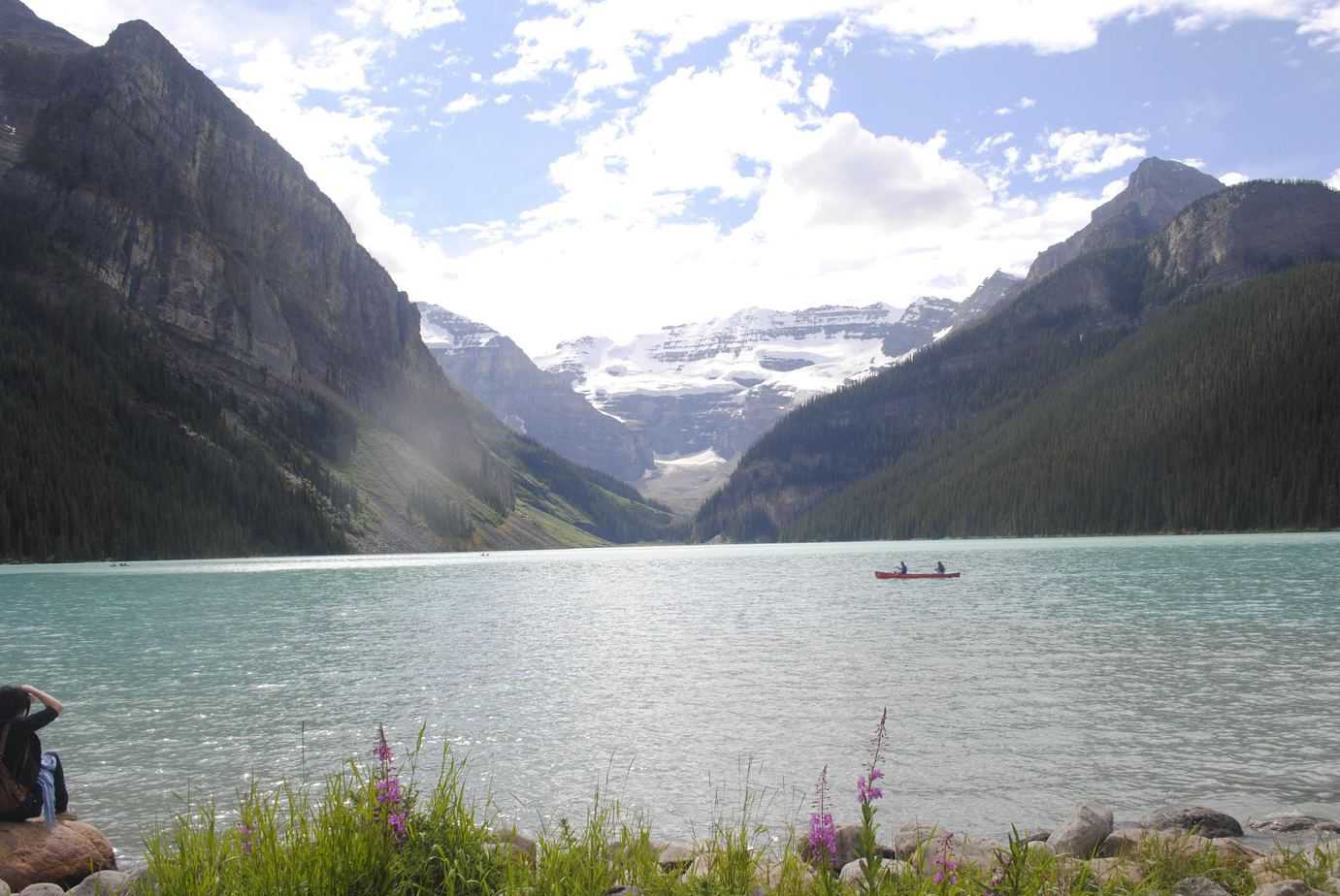 A couple is on a kayak in a river surrounded by mountains.