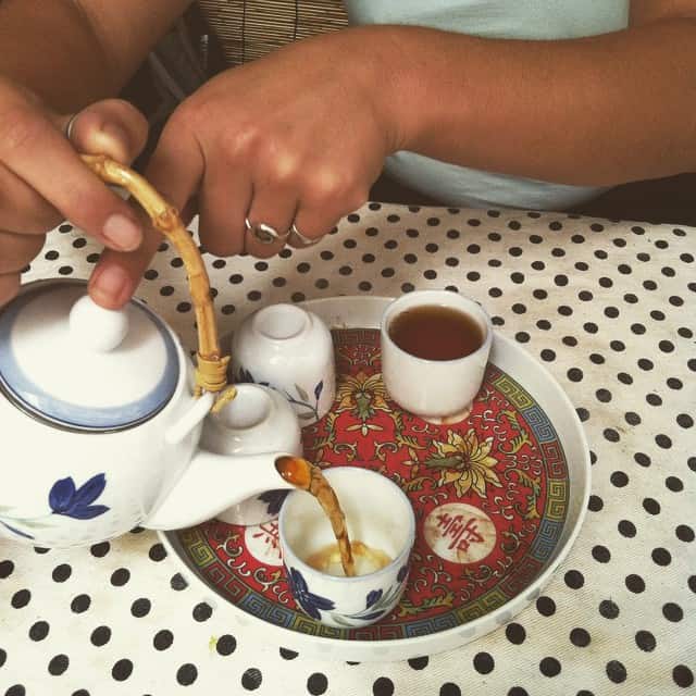 A woman pouring a cup of tea into a white cup on a table with black and white polka dots.