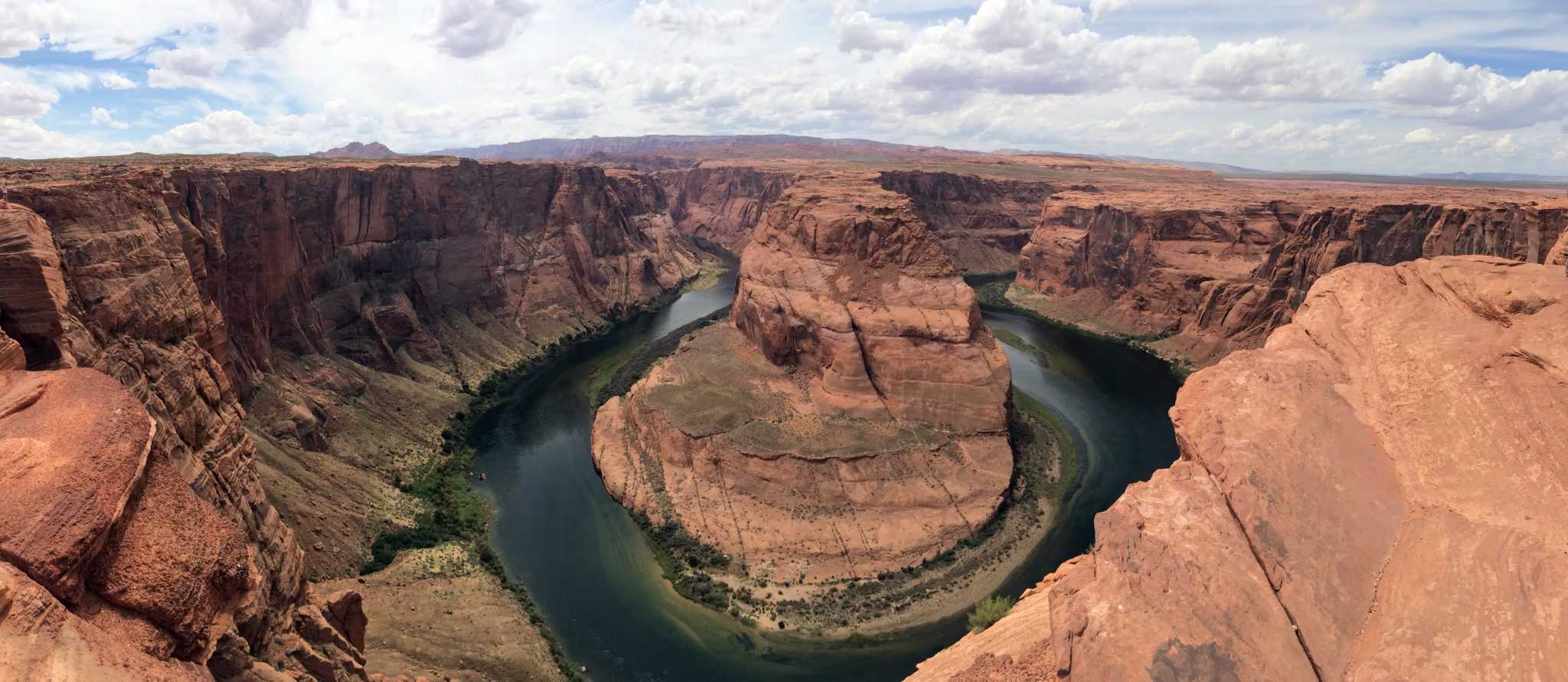 Horseshoe-shaped river bends around a tall red canyon under a blue sky.