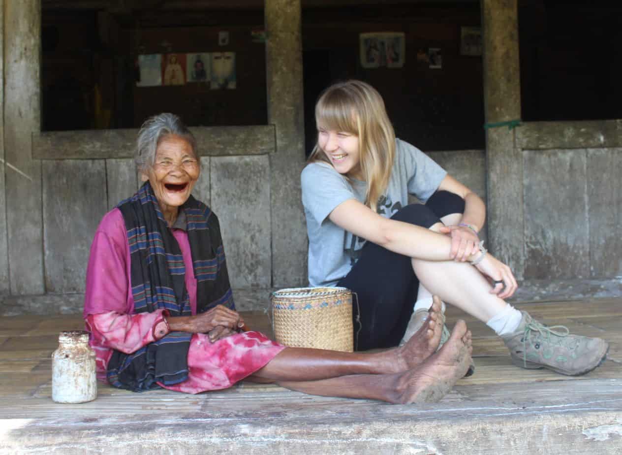 Two women sit laughing on the ground, with a woven basket sitting between them.