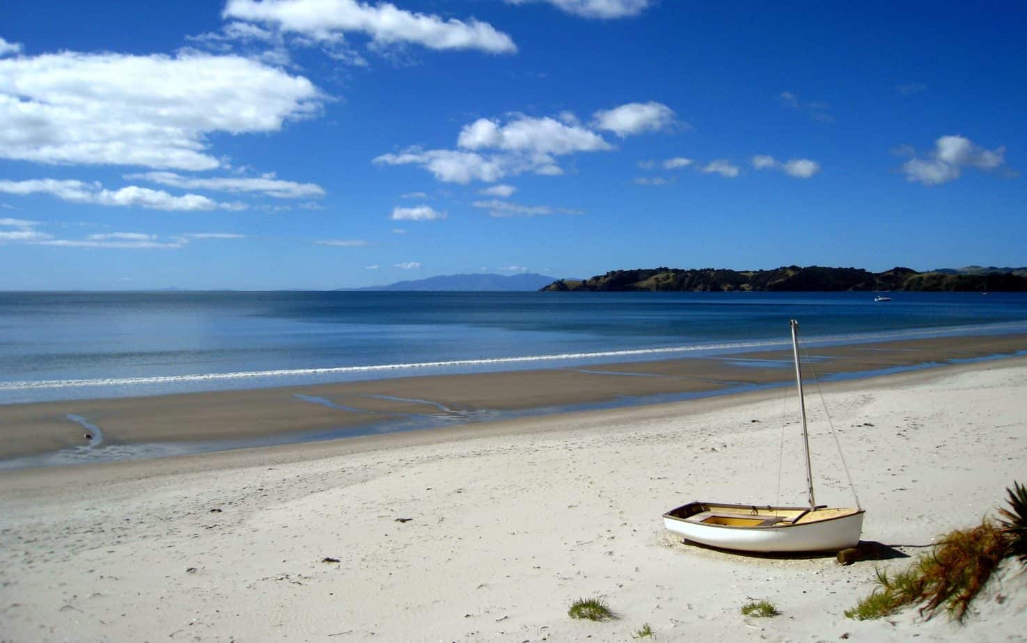 A white boat sits on a sandy beach with no people.