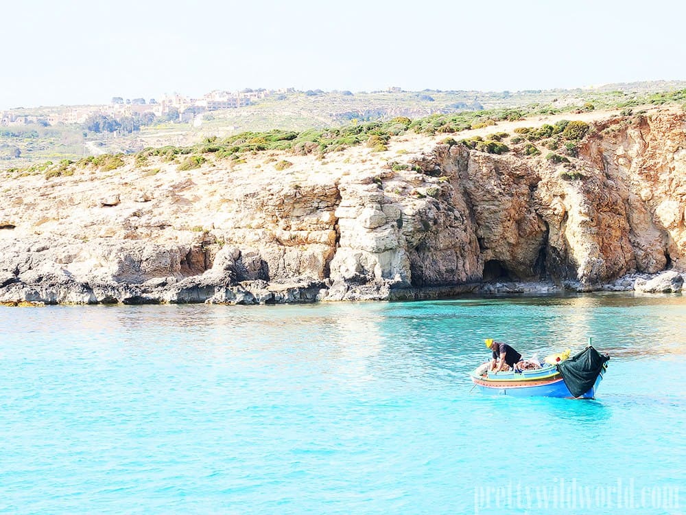 A blue boat floats on a blue body of water with rocky cliffs.