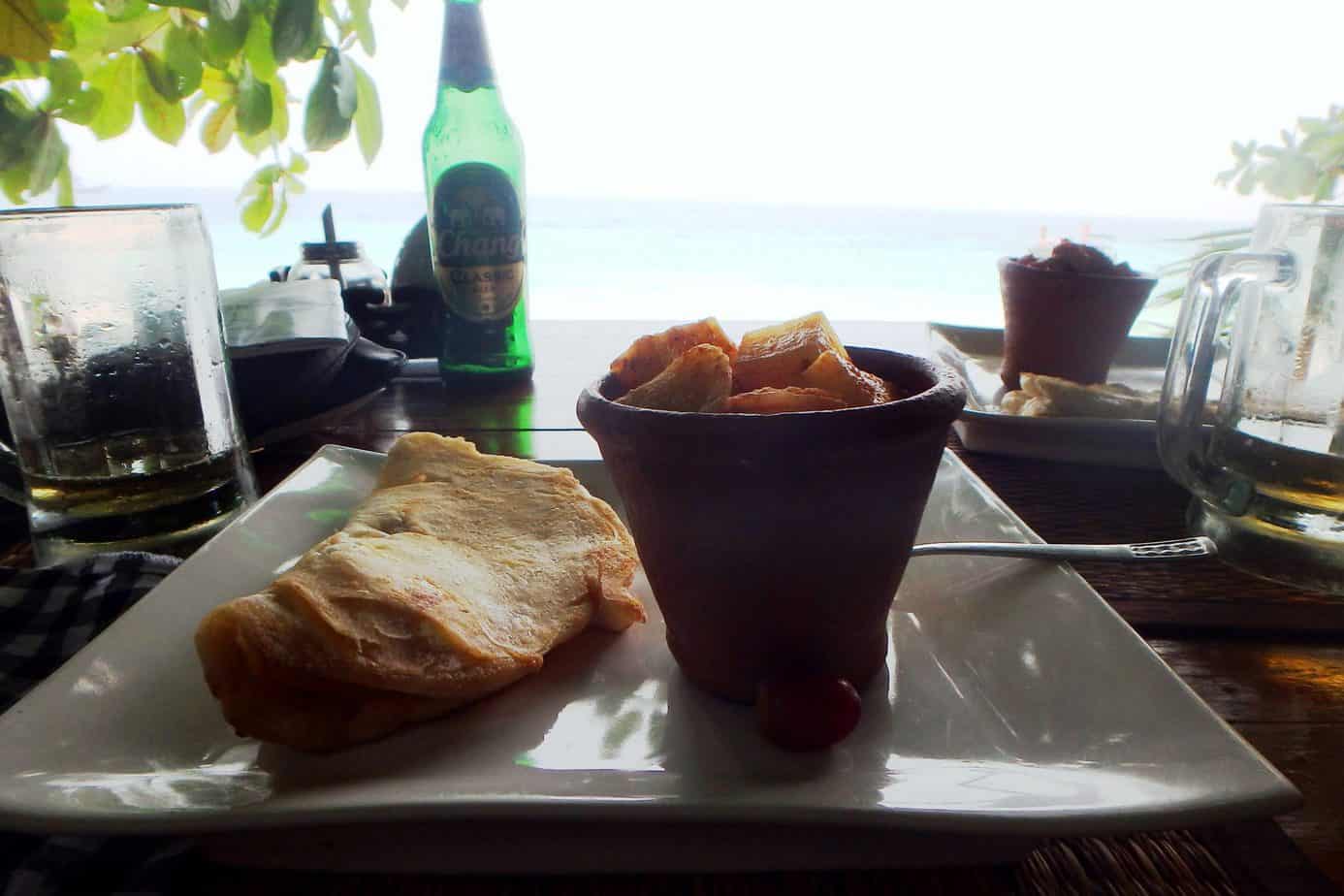 A plate of food with a green bottle behind it can be seen with water in the distance.