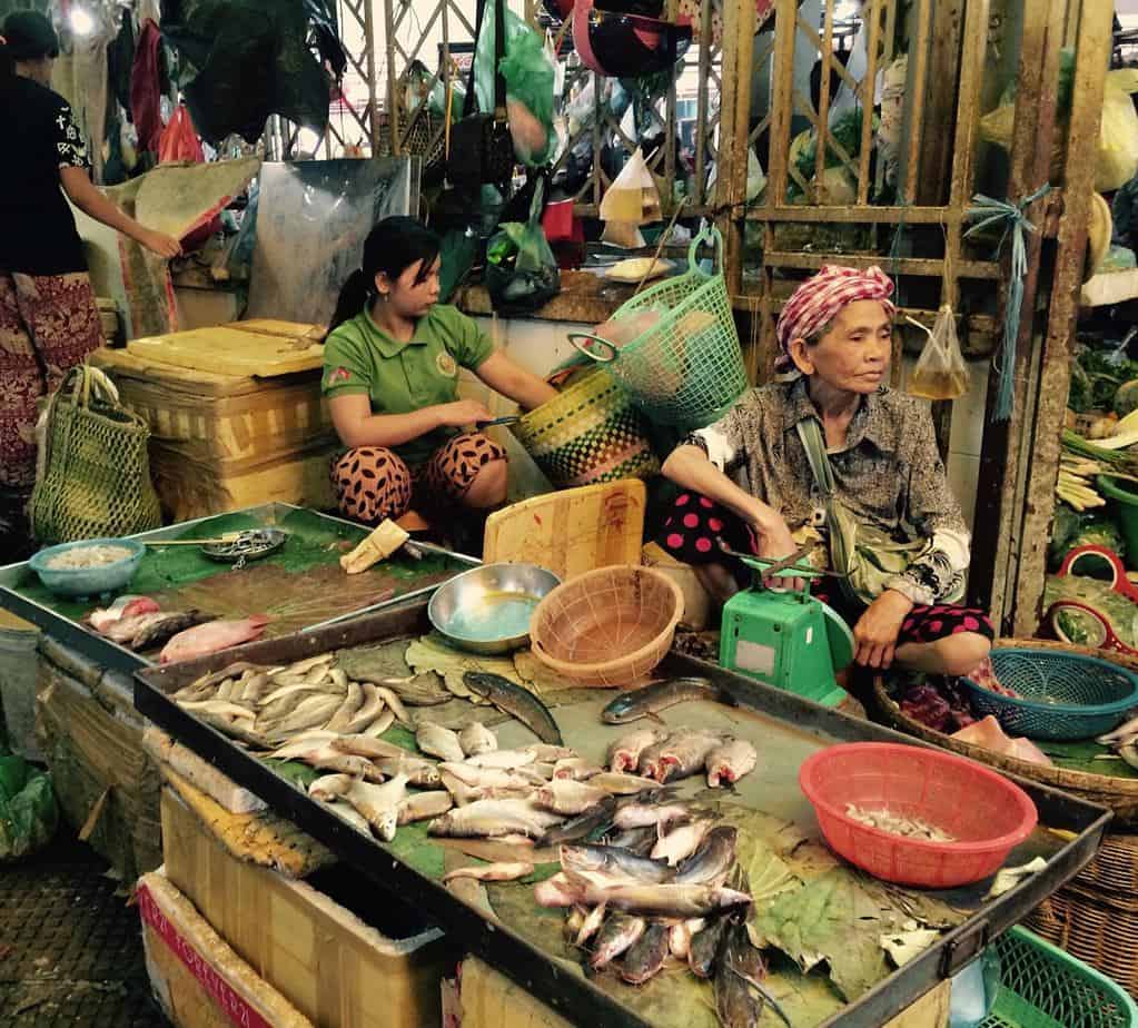 Women sit around an outdoor table with fish, working.