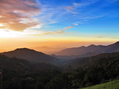 Aerial view of a scenic mountain range with greenery under a blue and orange sunset sky.