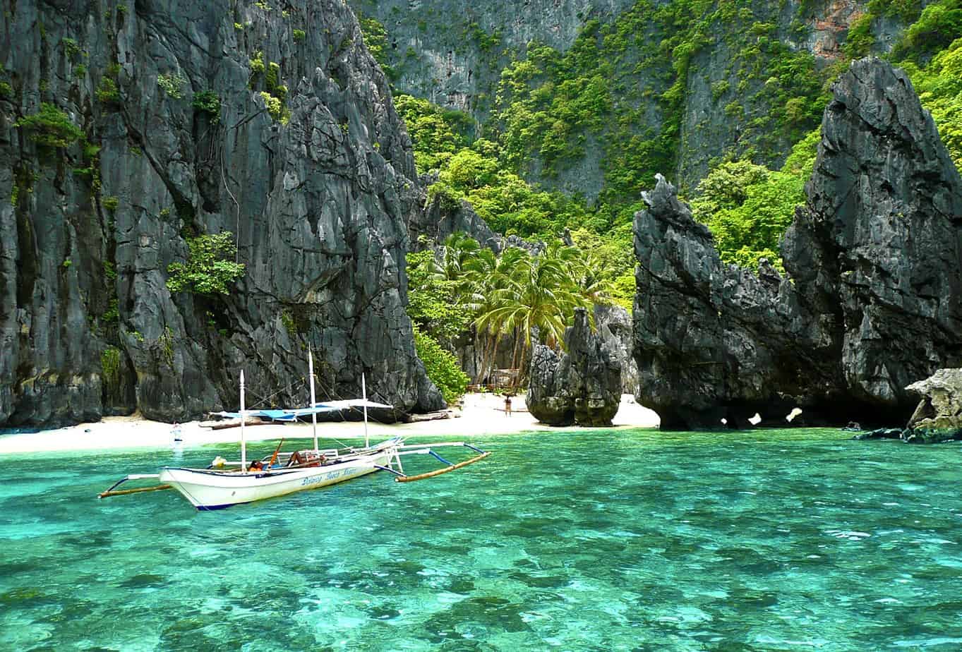 A boat floats on bright blue waters surrounded by tall rocky cliffs.