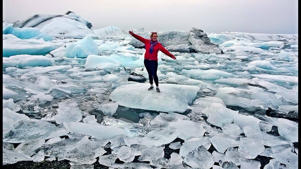 A woman stands on a giant piece of ice surrounded by water and more ice.