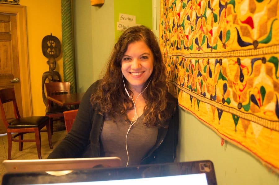 A woman sitting at a table with a laptop and smiling at the camera.