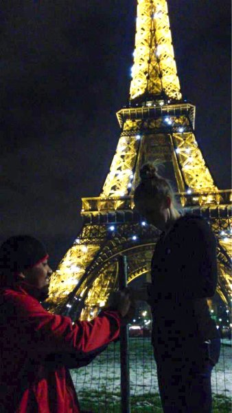 Man standing down on one knee while proposing to a woman next to the Eiffel Tower at night.
