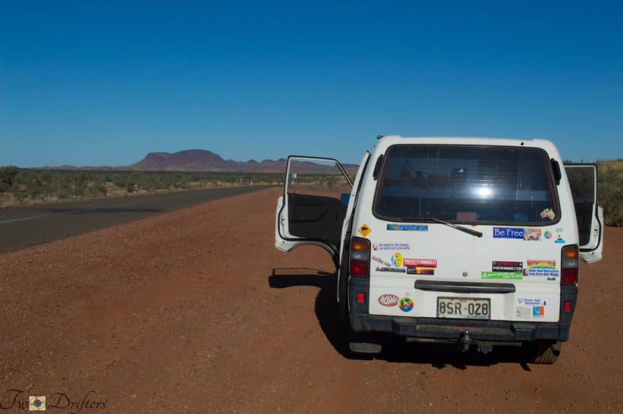 A white van with its door open and stickers on the back sits on a dirt road
