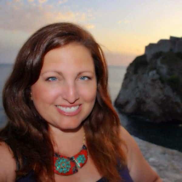 A woman smiles with a view of the sun setting over the beach behind her.