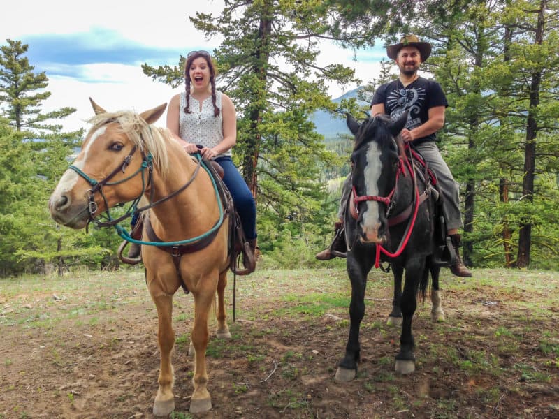 Husband and wife riding horses in the forest while laughing.