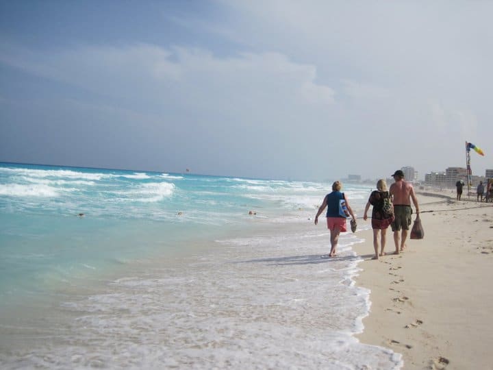 People walk along the edge of the water on the beach.
