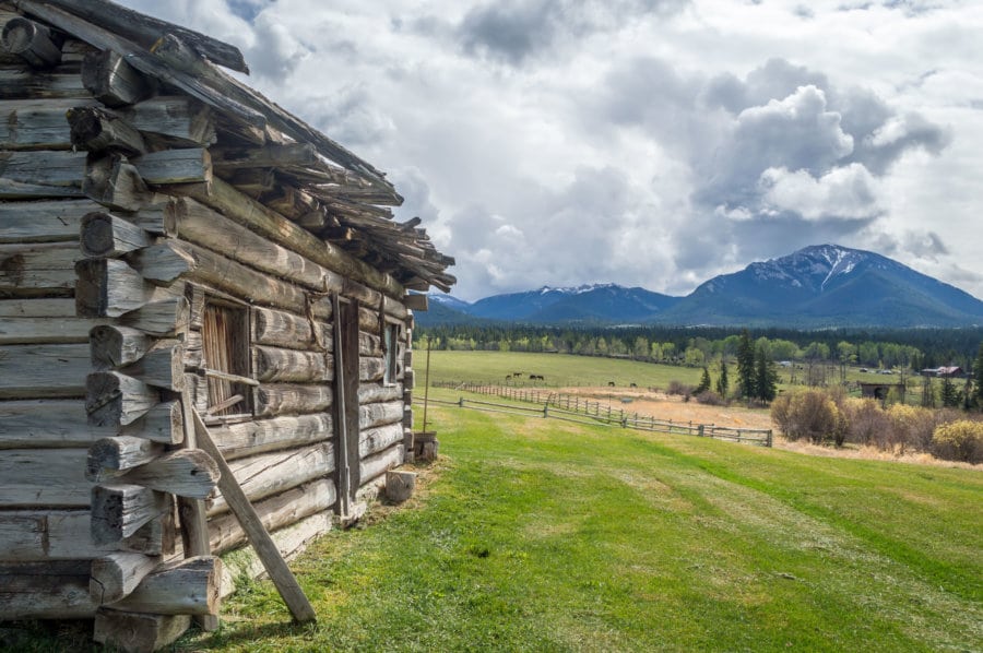 A log cabin next to a meadow with mountains in the background.