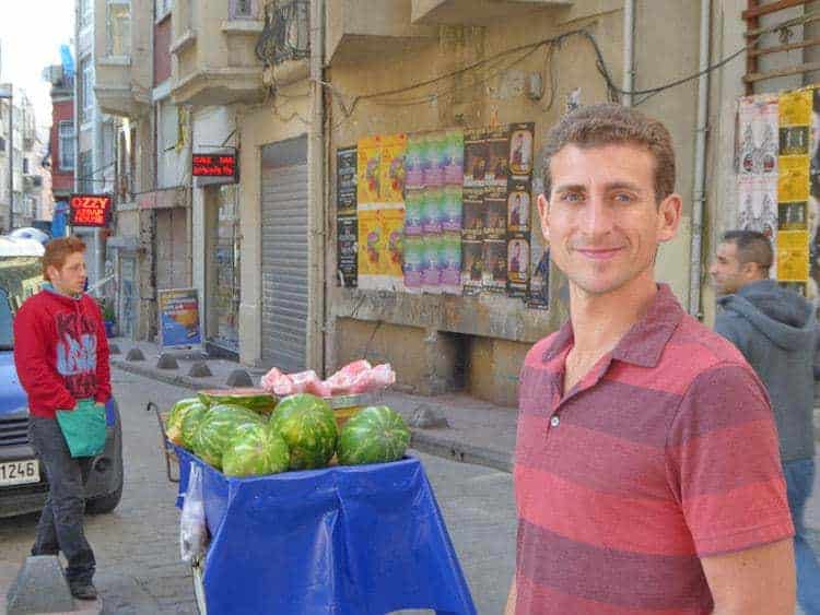A man smiles next to a stand with watermelon.