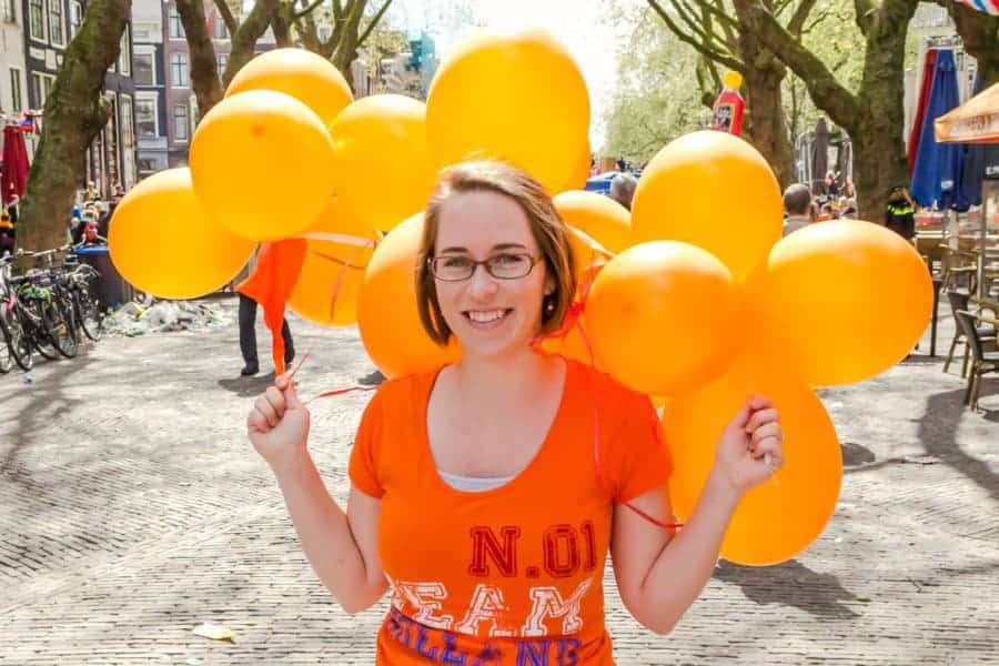 A girl in an orange shirt holds orange balloons.