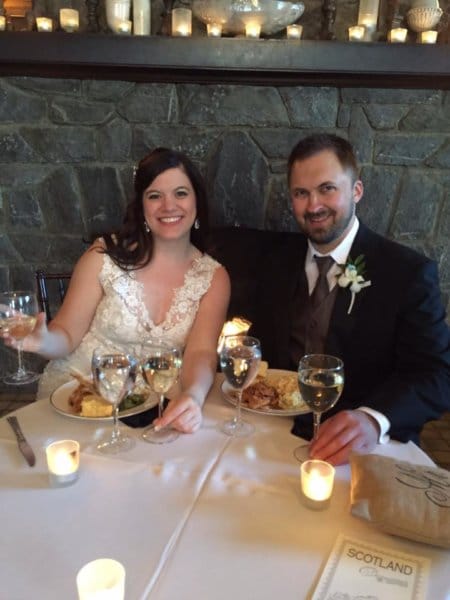 A couple sits at a table on their wedding day holding wine.