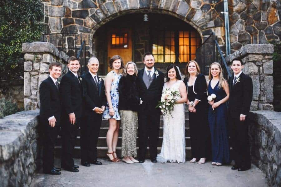 Family photo on a wedding day outdoors in front of a stone building.