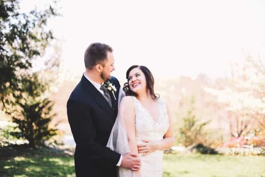 A bride and groom smile at each other outdoors.