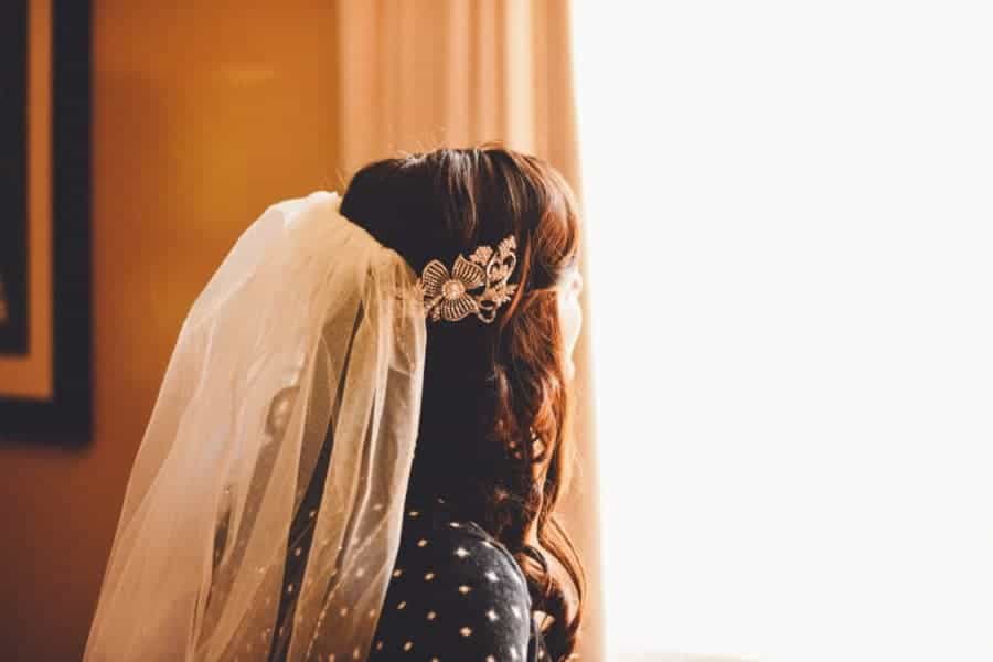 A woman looks out the window with her hair covered in a wedding veil.